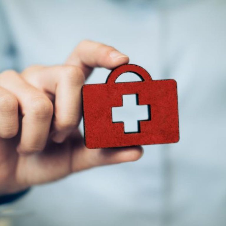 Red medical kit with a white cross, held by a person in a light-colored shirt.